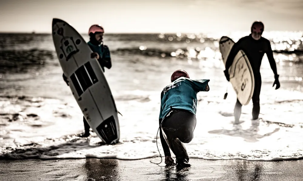 Three surfers running into the water at the beach with the "One More Wave" program